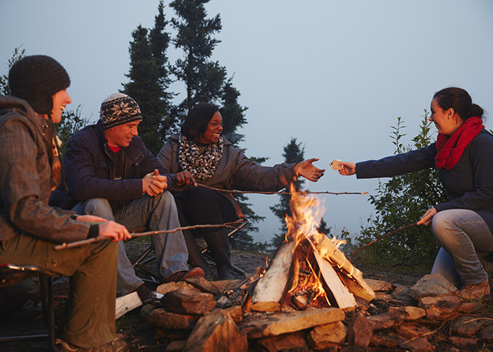 mixed group of friends talking and sharing food outdoors around a camp fire