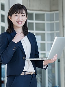 Asian woman in business suit smiling while holding a laptop