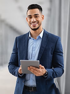 Latino man in business suit smiling while holding a tablet