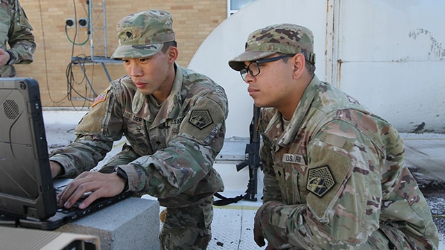 Two soldiers working on a laptop out in the field