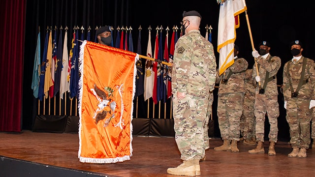 Soldiers on a stage holding the 60th OCO Signal Battalion flag